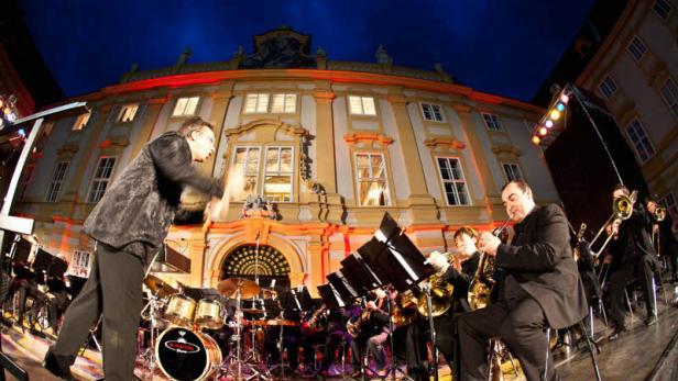 Ein Orchester spielt vor einem beleuchteten Gebäude bei Nacht.
