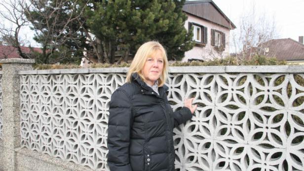 Eine Frau in Winterjacke steht vor einem gemusterten Betonzaun.