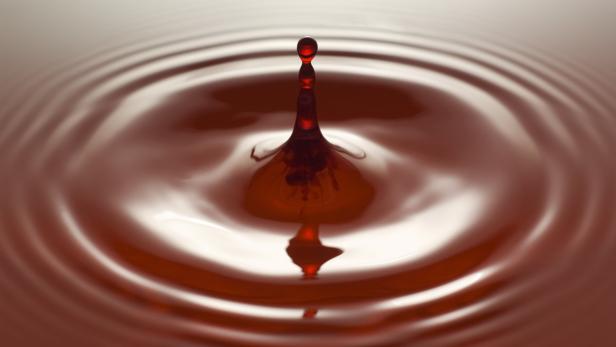 Ein roter Tropfen fällt in eine Flüssigkeit und erzeugt konzentrische Wellen.