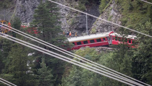 Ein entgleister roter Zug steht an einem Hang neben einer Felswand.