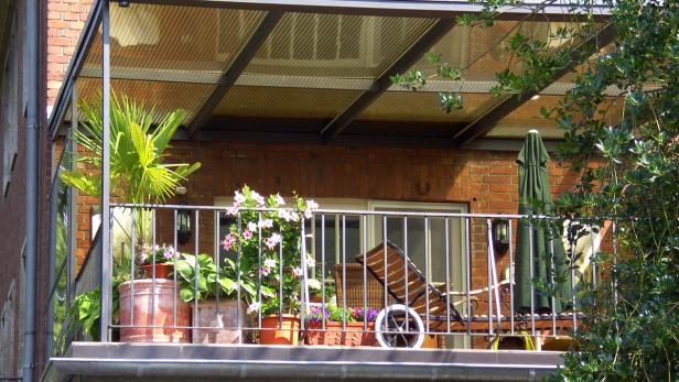 Ein Balkon mit Pflanzen, einem Sonnenschirm und einem Liegestuhl.