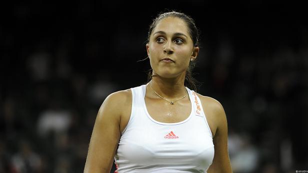 Eine Tennisspielerin in einem weißen Tanktop blickt konzentriert zur Seite.