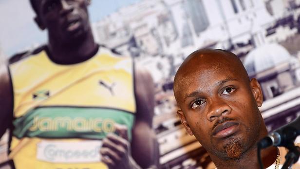 Asafa Powell posiert vor einem Poster von Usain Bolt.