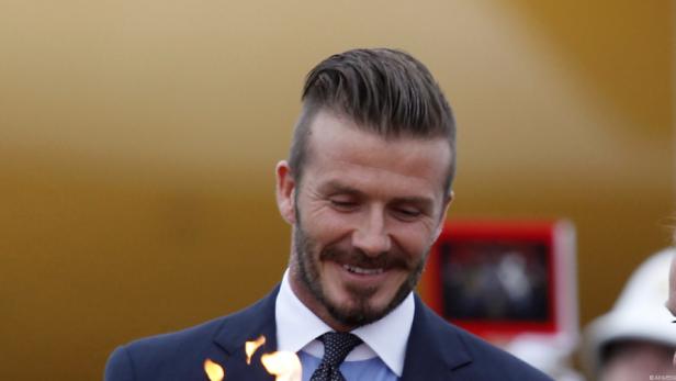 David Beckham lächelt in einem dunklen Anzug.