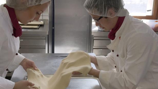 Zwei Köche in einer Küche bereiten Teig zu.