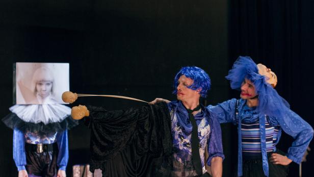 Drei Performer in Kostümen stehen auf einer Bühne.