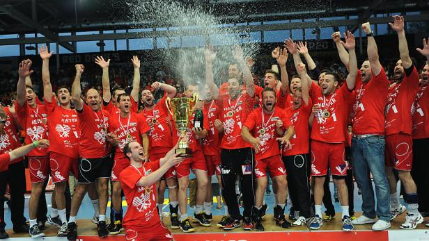 Eine Handballmannschaft feiert mit einem Pokal und Champagner den Sieg.