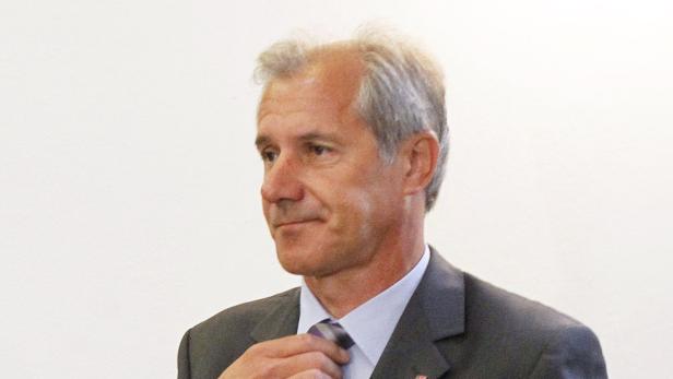 Ein Mann mit grauem Haar und Anzug richtet seine Krawatte.