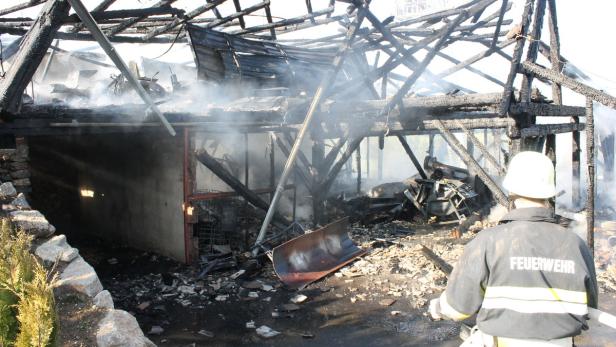 Ein Feuerwehrmann steht vor einem ausgebrannten Gebäude, aus dem Rauch aufsteigt.