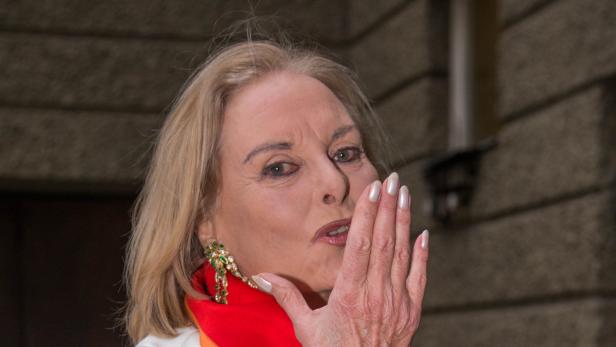 Eine Frau mit blonden Haaren und auffälligem Ohrschmuck hält ihre Hand vor das Gesicht.