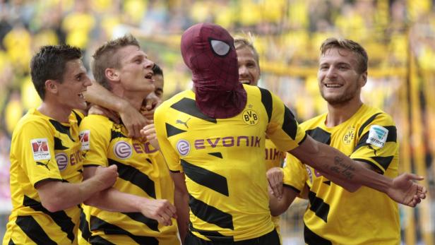 Ein Fußballspieler mit einer Spider-Man-Maske wird von seinen Teamkollegen umarmt.