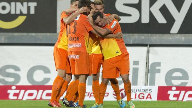 Eine Gruppe Fußballspieler in orangefarbenen Trikots umarmt sich auf dem Spielfeld.