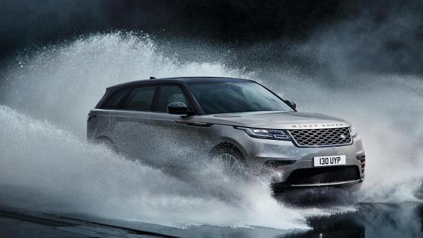 Ein silberner Range Rover Velar fährt durch eine Wasserfontäne.