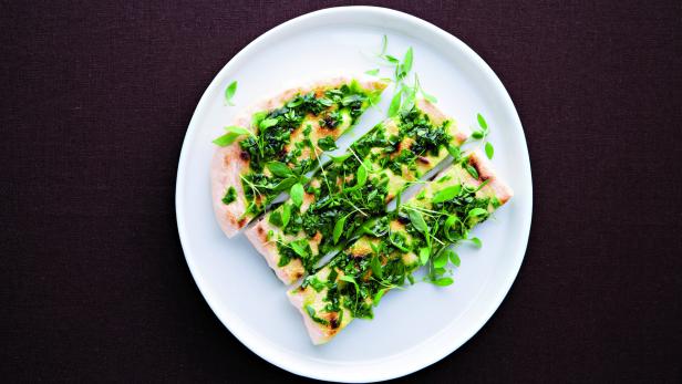 Eine geschnittene Pizza, belegt mit grünen Kräutern, auf einem weißen Teller.