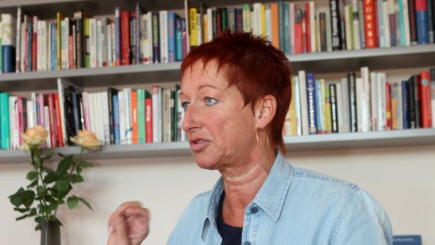 Eine Frau mit roten Haaren spricht vor einem Bücherregal.
