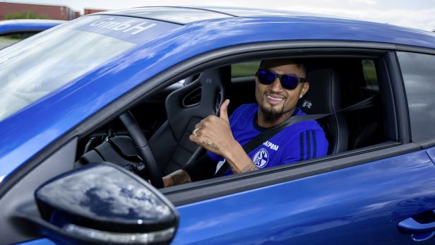 Ein Mann mit Sonnenbrille sitzt in einem blauen Auto und zeigt den Daumen nach oben.