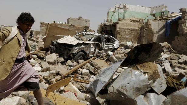 Ein Junge steht vor einem zerstörten Auto und Trümmern eines Gebäudes.