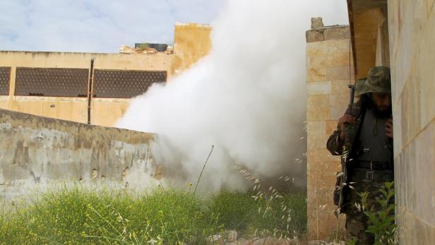 Ein Soldat in Tarnkleidung steht in einem Gebäude, während Rauch aus einem anderen Gebäude dringt.