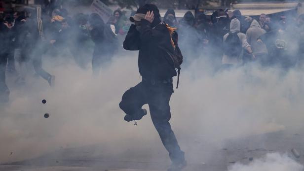 Eine Person rennt durch eine Rauchwolke, während im Hintergrund eine Menschenmenge zu sehen ist.