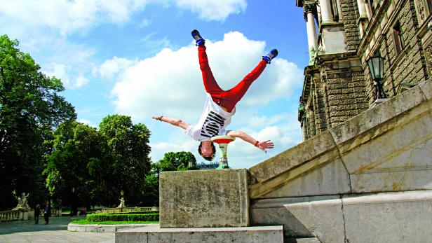 Ein Mann macht einen Handstand auf einem Podest vor einem Gebäude.