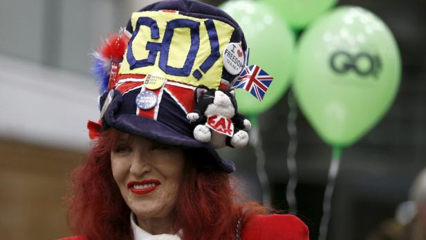 Eine Frau mit rotem Haar trägt einen auffälligen Hut mit politischer Botschaft und einer kleinen Katzenpuppe.