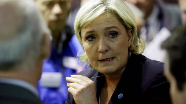 Marine Le Pen steht schräg gegenüber von einem Mann der vorn eine Glatze und hinten ein paar weiße Haare hat und hat eine schwarze Weste an