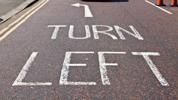 Auf der Straße ist eine Markierung „Turn Left“ mit einem Pfeil nach links angebracht.