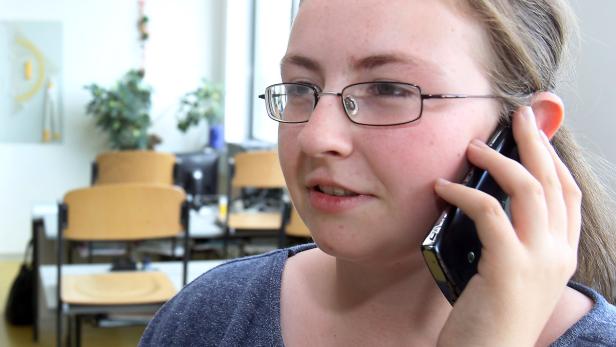 Eine junge Frau mit Brille telefoniert in einem Büro.