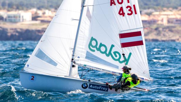 Ein Segelboot mit österreichischer Flagge und zwei Personen an Bord auf dem Wasser.
