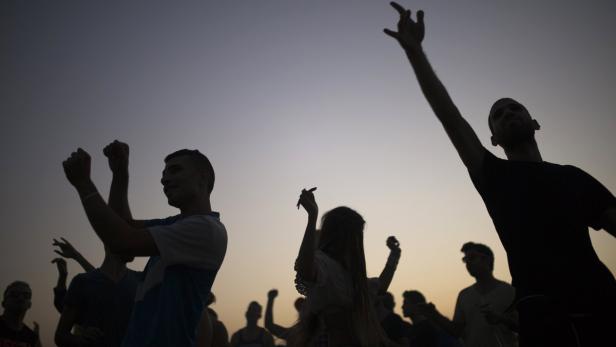 Eine Gruppe von Menschen tanzt bei Sonnenuntergang als Silhouette.