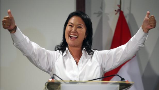 Keiko Fujimori lächelt und zeigt beide Daumen nach oben vor einer peruanischen Flagge.