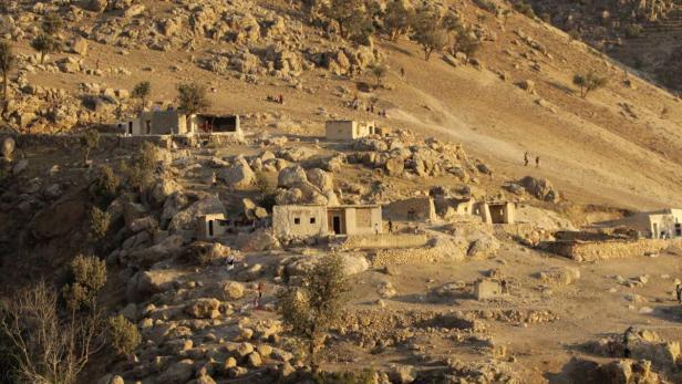 Eine Siedlung mit einfachen Häusern liegt an einem sonnigen, felsigen Hang.