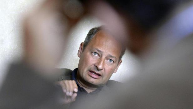 Ein Mann mit Anzug schaut durch einen unscharfen Vordergrund in die Kamera.