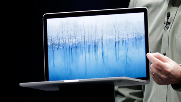 Ein Mann präsentiert ein MacBook mit einem Bild von Bäumen im Wasser.