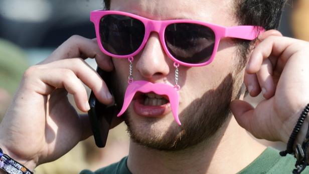 Ein Mann mit pinkfarbener Sonnenbrille und Schnurrbart-Accessoire telefoniert.