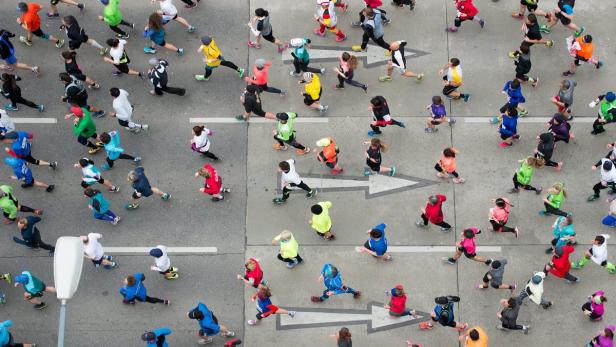 Eine Menschenmenge läuft einen Marathon auf einer asphaltierten Straße mit Pfeilmarkierungen.
