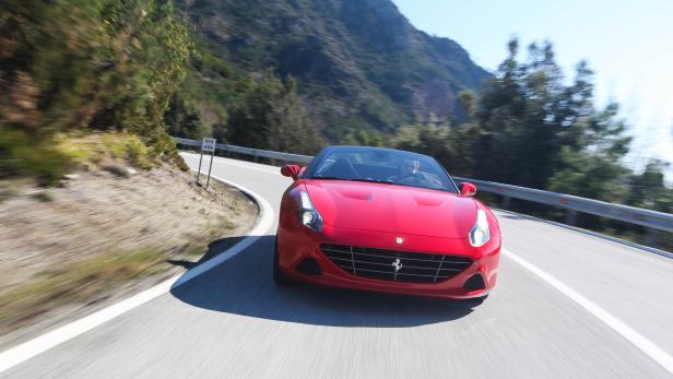 Ein roter Ferrari fährt auf einer kurvenreichen Straße in den Bergen.