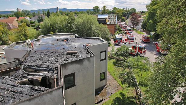Nach einem Brand stehen mehrere Feuerwehrautos vor einem beschädigten Gebäude.