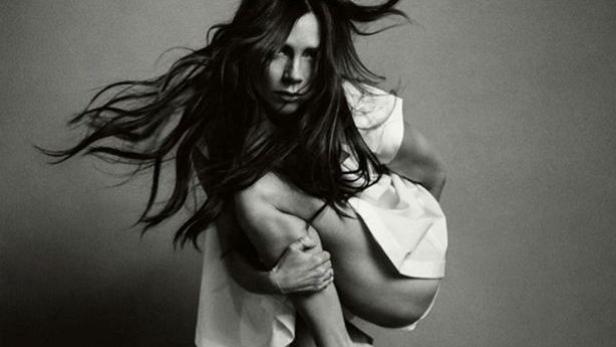 Eine Frau in einem weißen Kleid kauert mit wehendem Haar.