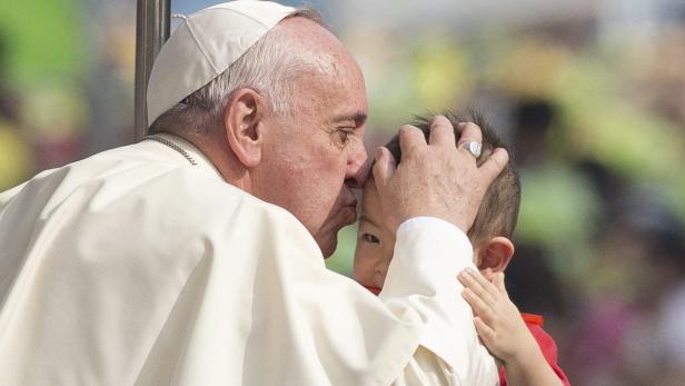 Papst Franziskus küsst ein Kind auf die Stirn.