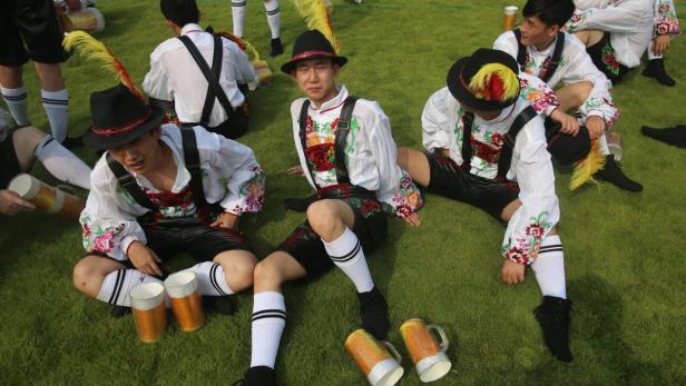 Eine Gruppe junger Männer in Tracht sitzt auf einer Wiese mit Bierkrügen.