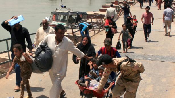 Menschen, darunter Kinder, werden von einem Soldaten in einer Schubkarre über eine Brücke gebracht.
