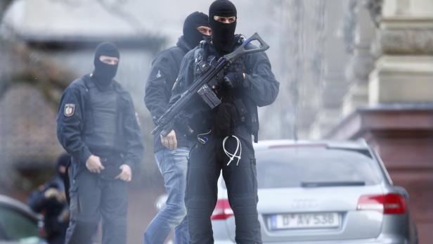Mehrere Polizisten in Kampfmontur und mit Sturmhauben stehen vor einem Gebäude.