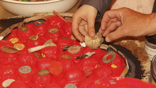 Zwei Personen gestalten ein Kunstwerk mit roter Farbe und verschiedenen Objekten.