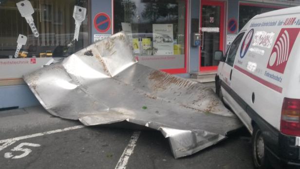 Ein großes, zerknittertes Blech liegt vor einem Geschäft für Sicherheitstechnik und einem Lieferwagen.