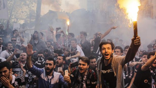 Eine Menschenmenge jubelt und zündet Bengalos, während Rauch in der Luft liegt.