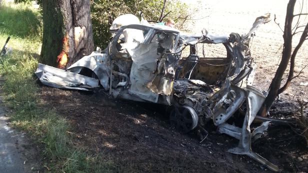 Ein ausgebranntes Auto liegt neben einem Baum.