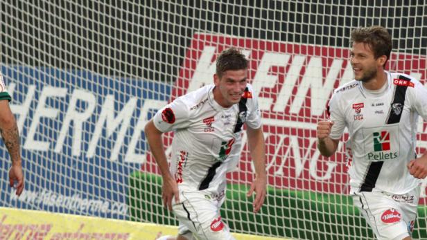 Zwei Fußballspieler jubeln vor dem Tornetz, ein dritter Spieler steht abseits.