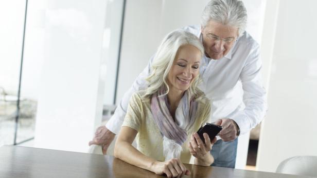 Ein älteres Paar schaut gemeinsam auf ein Smartphone am Tisch.