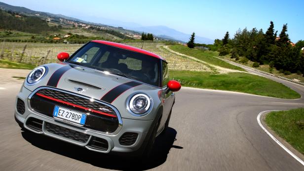 Ein grauer Mini Cooper mit rotem Dach fährt auf einer kurvenreichen Straße.